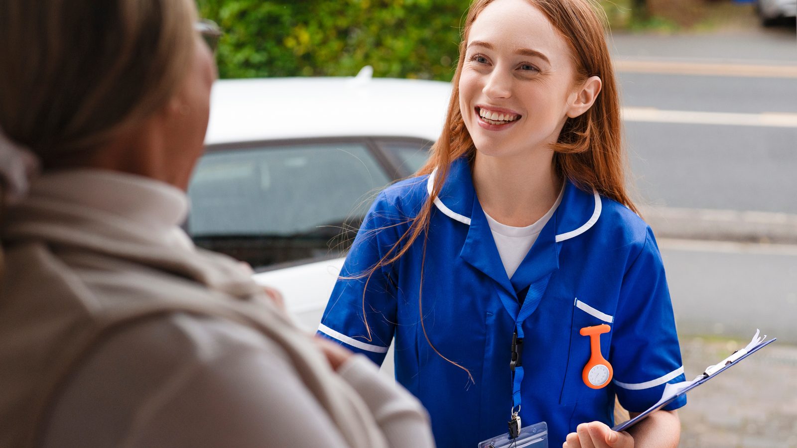 A community nurse with a clipboard talking with someone at the door of a home visit